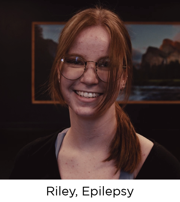 Young woman with red hair and glasses smiles at the camera