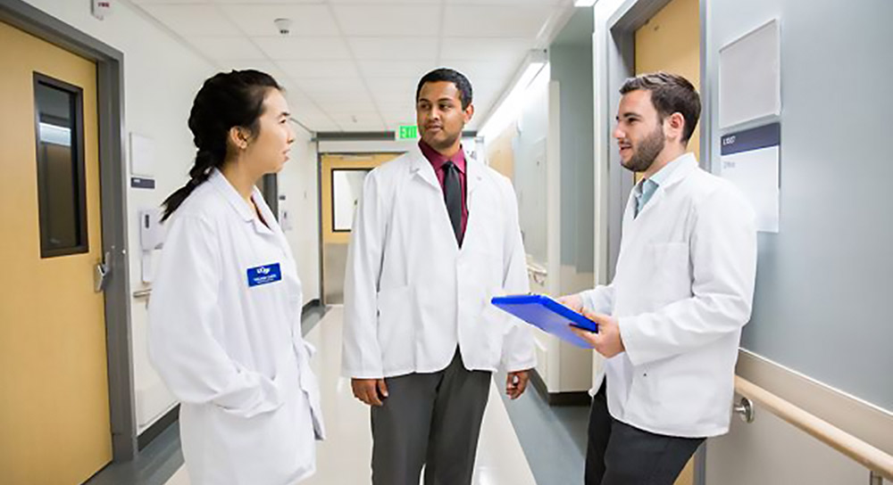 Three residents, a female and two males, stand in a hospital hallway