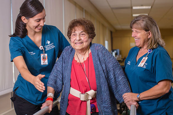 A mature woman is being aided in using her walker by two female healthcare workers