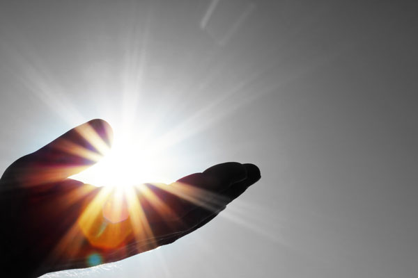 A close up of a hand in shadow. The sun reflects in the background so it looks like the palm is holding sunlight.