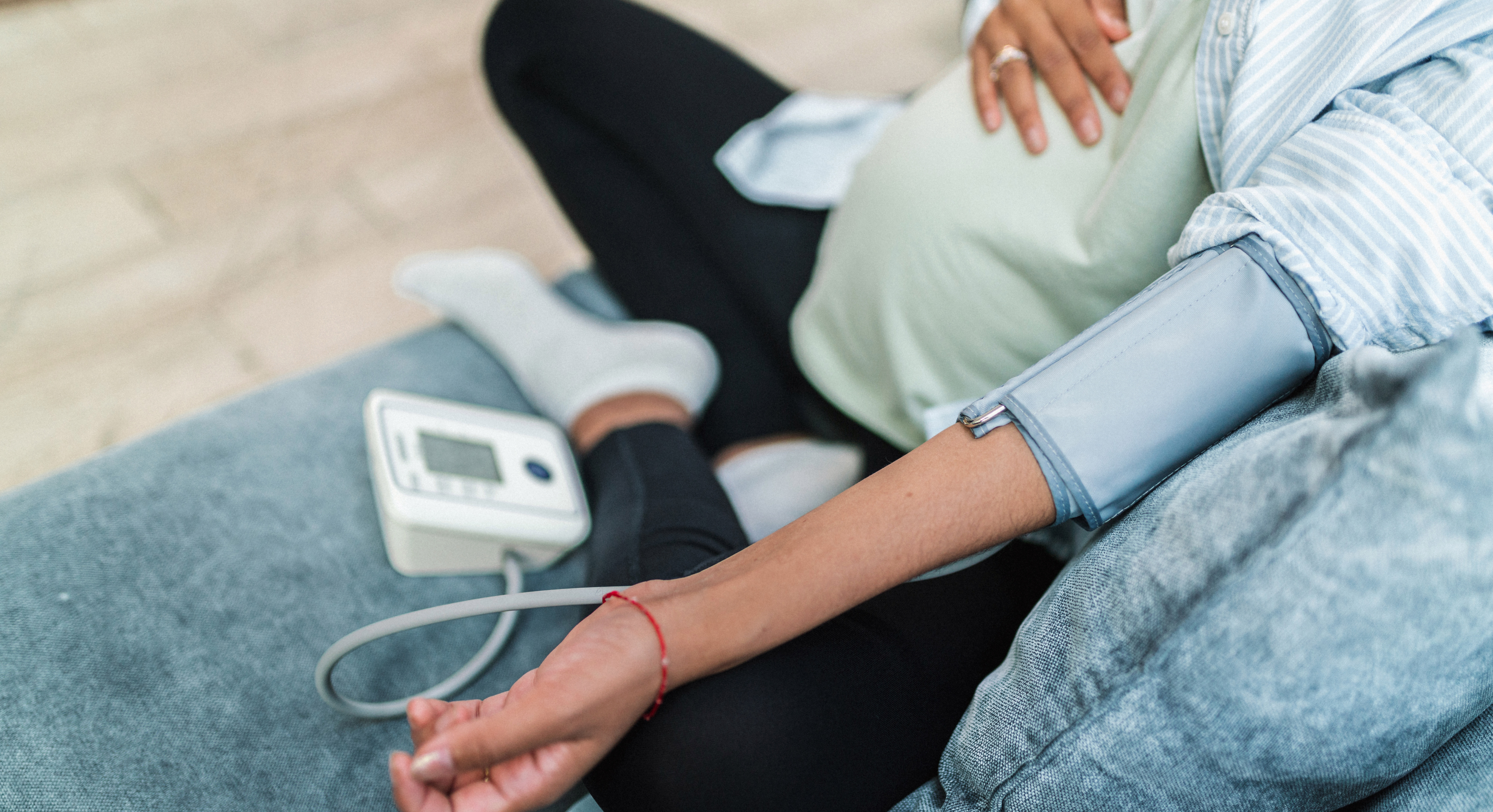 The abdomen of a pregnant woman sitting on a couch is shown. A blood pressure cuff is on her arm and a monitor sits on the couch next to her.