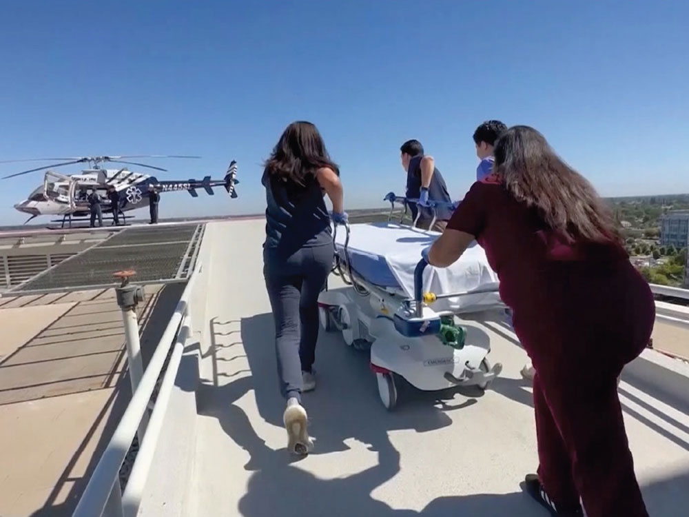 A group of five responders push a gurney toward an arriving helicopter