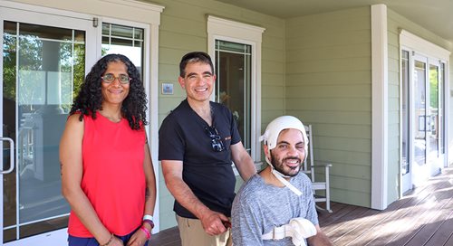 Netzer and Sagit Peled stand near their son, Gev, who is in a wheelchair, on the porch of Terry's House. All three are smiling.