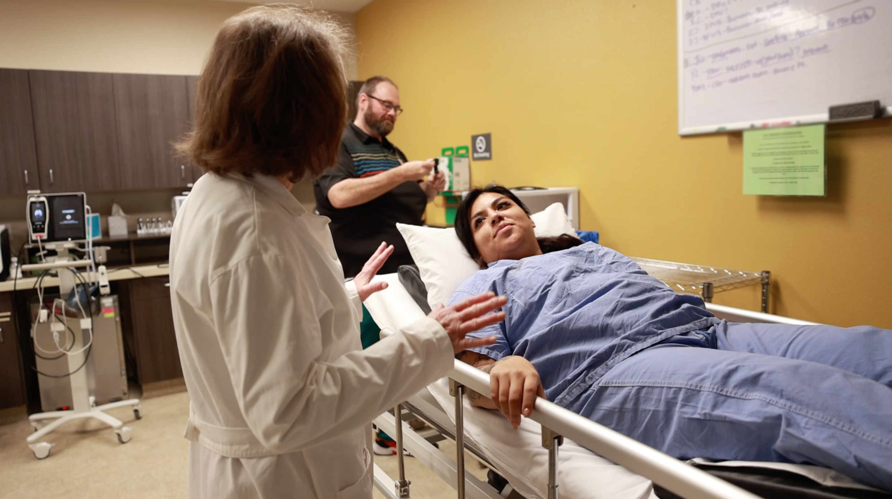 A female patient in a hospital bed looks up at her female doctor, who is preparing her for hyperbaric oxygen treatment