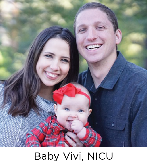 A young man and woman, both white, smile at the camera with their baby girl in between them